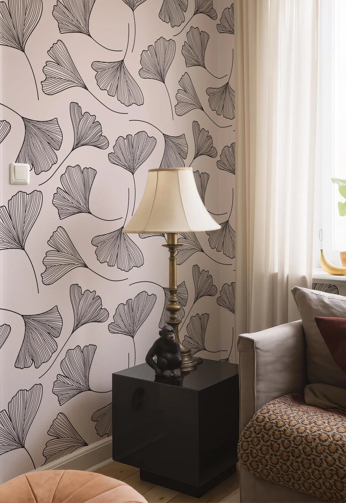 a living room with a black and white patterned wallpaper, a lamp on a black side table, and a beige sofa with a patterned throw pillow.