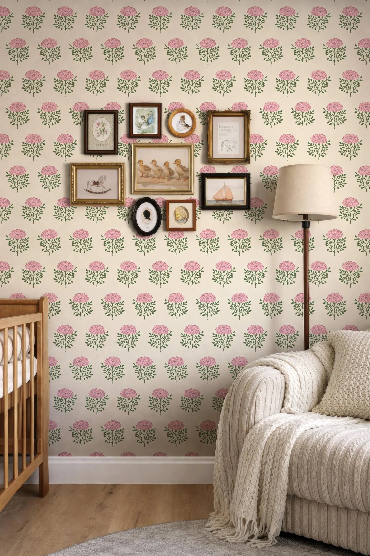 a cozy living room with a white sofa, a wooden rocking chair, and a lamp. The walls are decorated with a floral wallpaper pattern, and there are several framed pictures and photographs arranged on the wall.