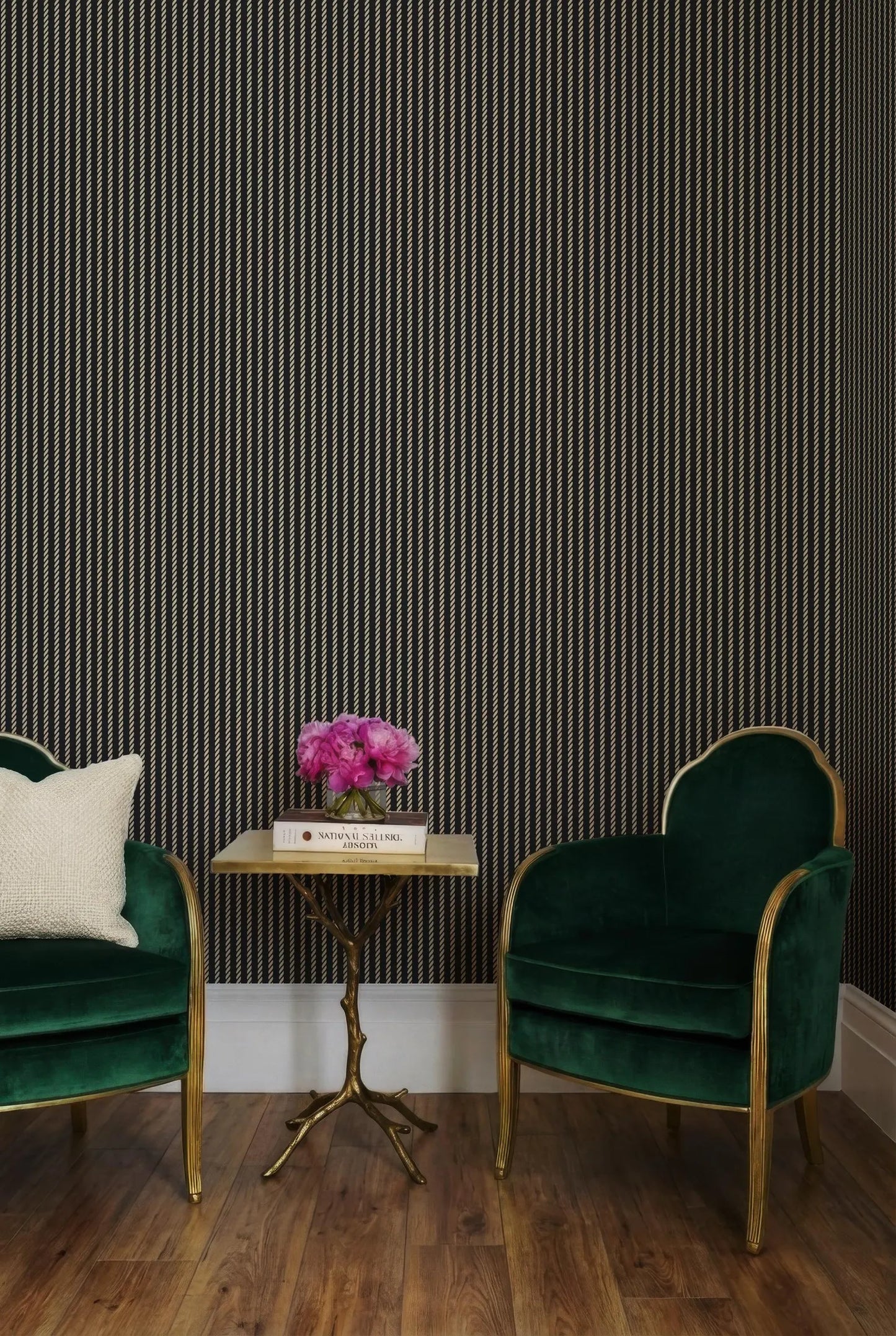 a cozy seating area with two green velvet armchairs and a small side table with a vase of pink flowers. The wall behind the seating area has vertical stripes in black and white.