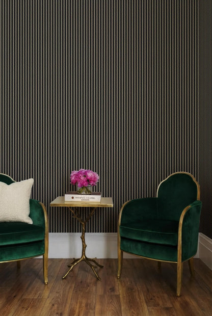 a cozy seating area with two green velvet armchairs and a small side table with a vase of pink flowers. The wall behind the seating area has vertical stripes in black and white.