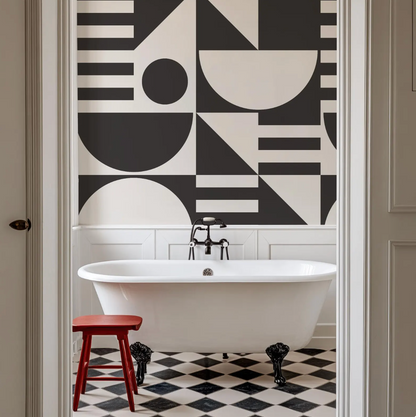a bathroom with a white freestanding bathtub, a red stool, and a black and white geometric pattern on the wall behind the bathtub.
