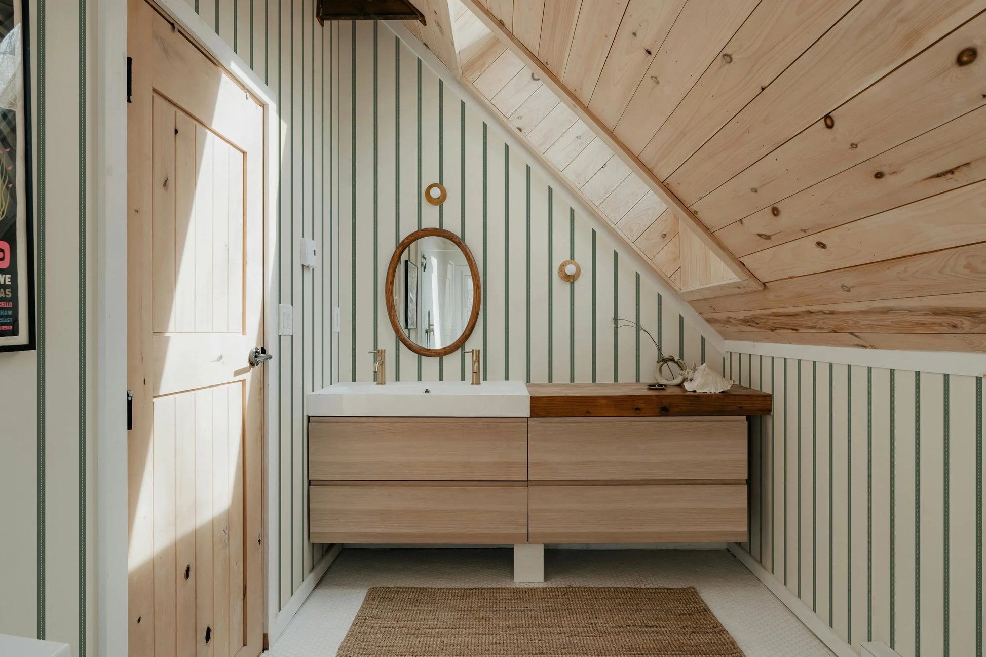 a modern bathroom with a wooden vanity and a large mirror above it. The bathroom has a slanted ceiling and wooden walls, creating a warm and cozy atmosphere.