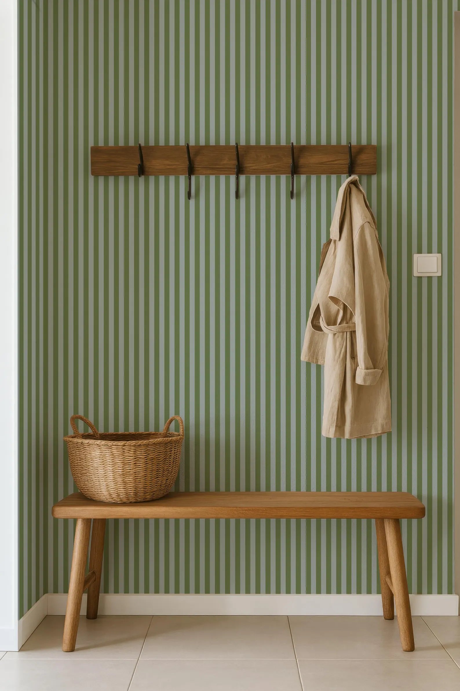 a wooden bench with a wicker basket on it, placed against a green and white striped wall with a coat rack hanging above it.