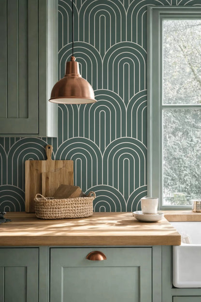 a kitchen with a wooden countertop, a woven basket, a wooden cutting board, and a copper pendant light. The kitchen has green cabinets and a patterned wallpaper, creating a cohesive and stylish design.