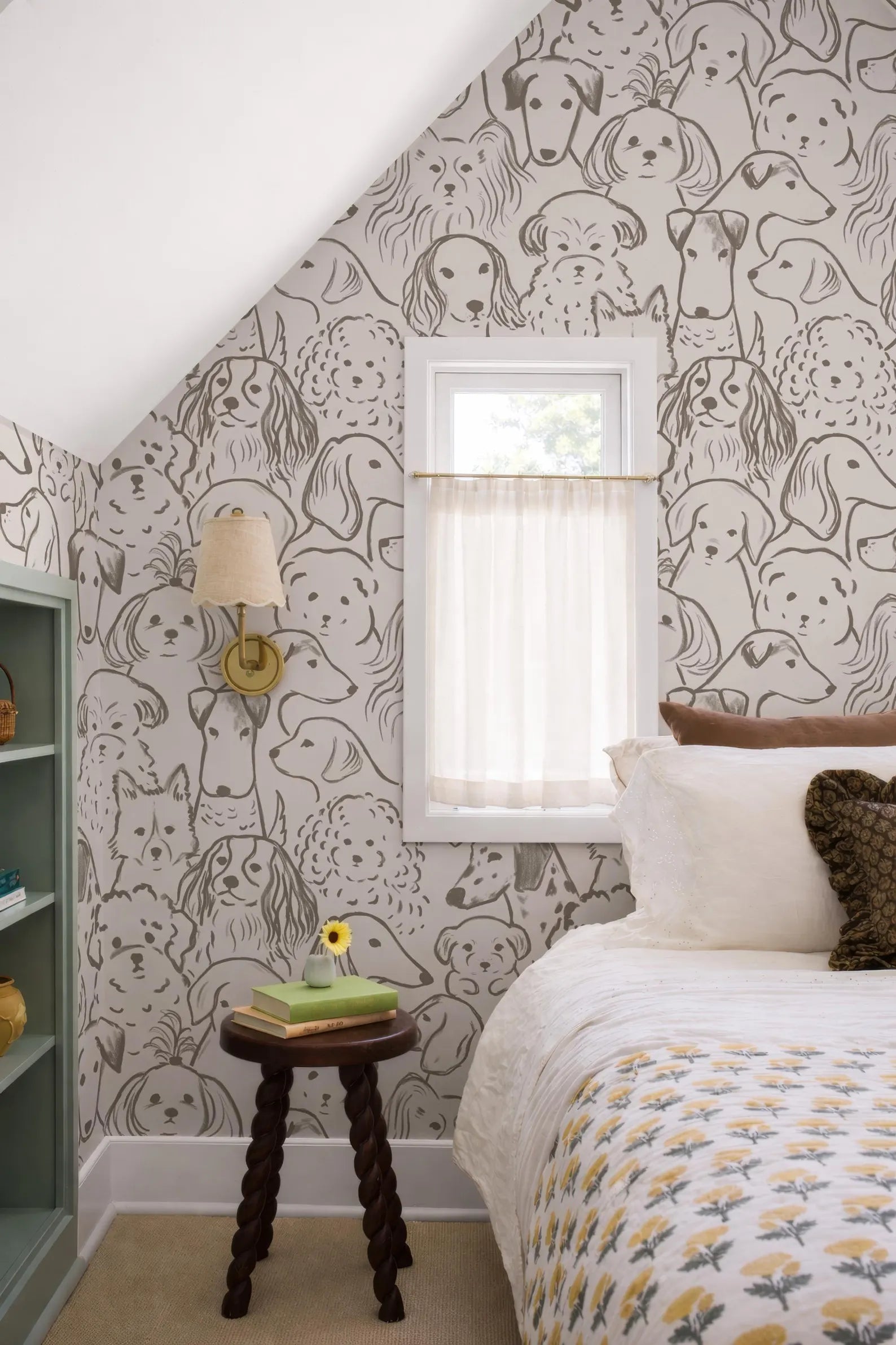 a bedroom with a bed, a small table, and a window with a white curtain. The wall behind the bed has a repeating pattern of dog faces, creating a unique and playful atmosphere.