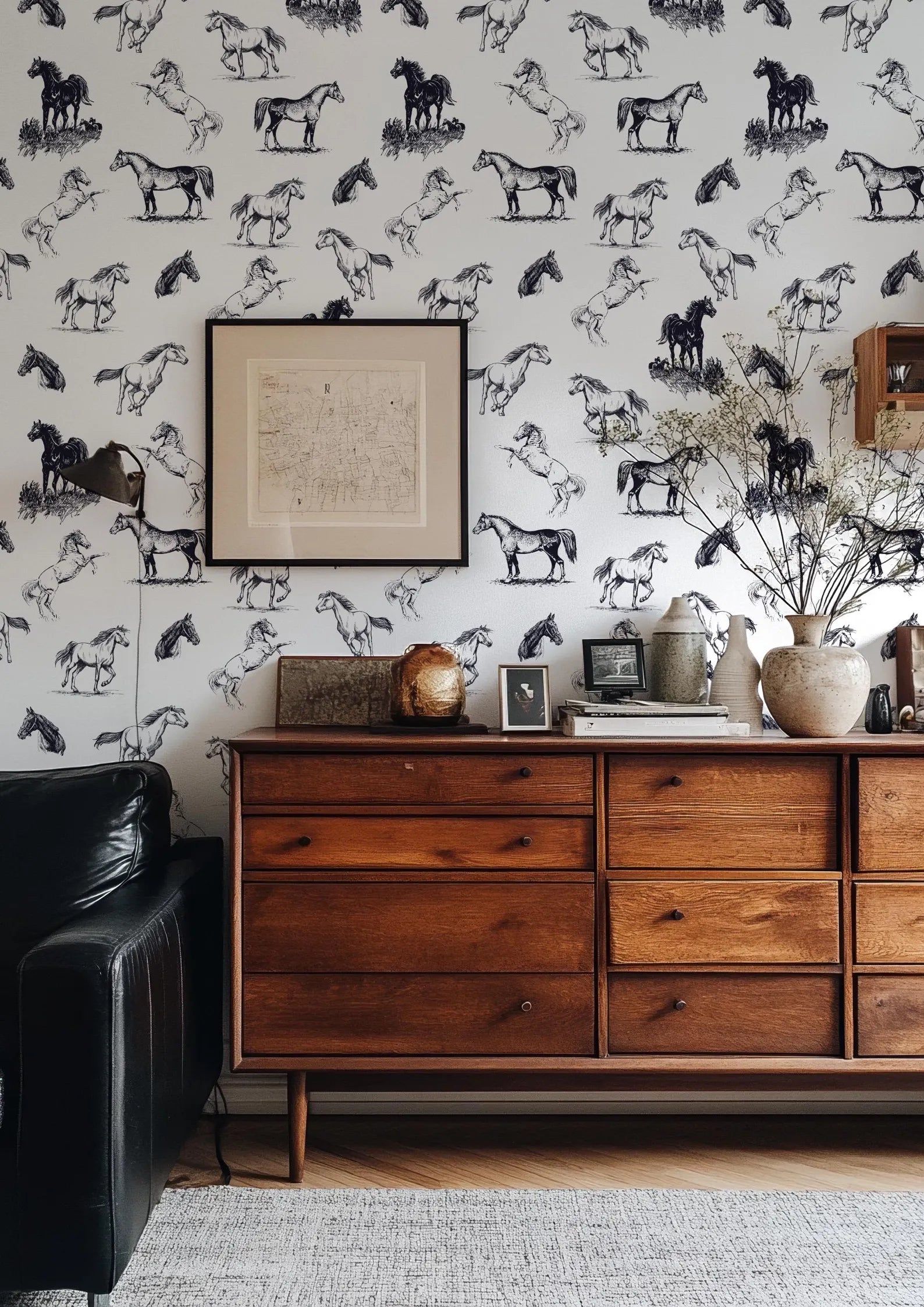 a wallpapered wall with a wooden dresser and a black leather couch in a living room setting.