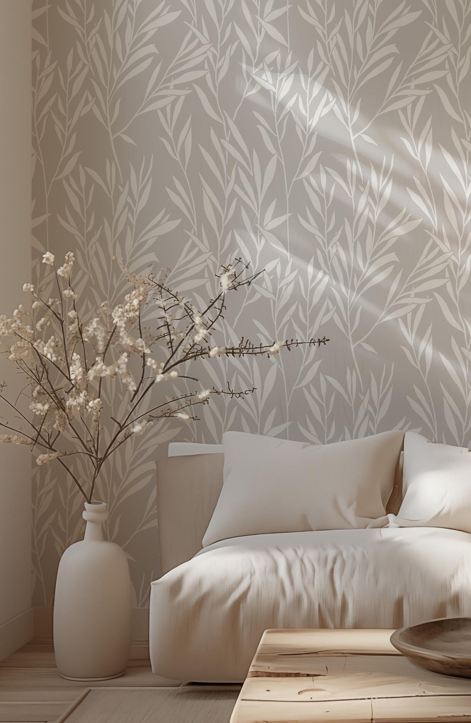 a cozy living room with a white sofa, a wooden coffee table, and a vase of white flowers on the floor. The room has a neutral color palette with a gray and white patterned wallpaper, creating a warm and inviting atmosphere.