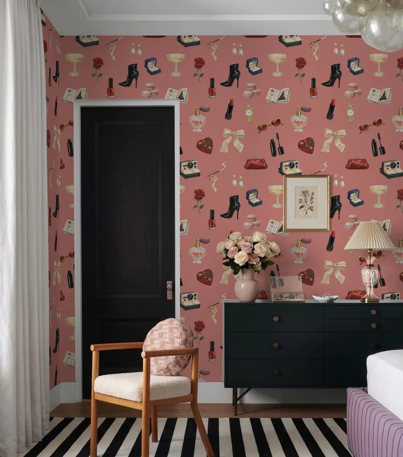 a bedroom with a pink wall adorned with a pattern of various objects, including shoes, books, and a vase. A black door is visible on the left side of the room, and a wooden chair is placed in front of the door. A dresser with a mirror is situated on the right side of the room, and a lamp is positioned on the right side of the dresser.