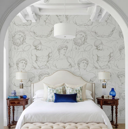 a bedroom with a large bed, white bedding, and a wallpapered wall with a repeating pattern of nude male figures. The room has a white archway and two nightstands with lamps on either side of the bed.