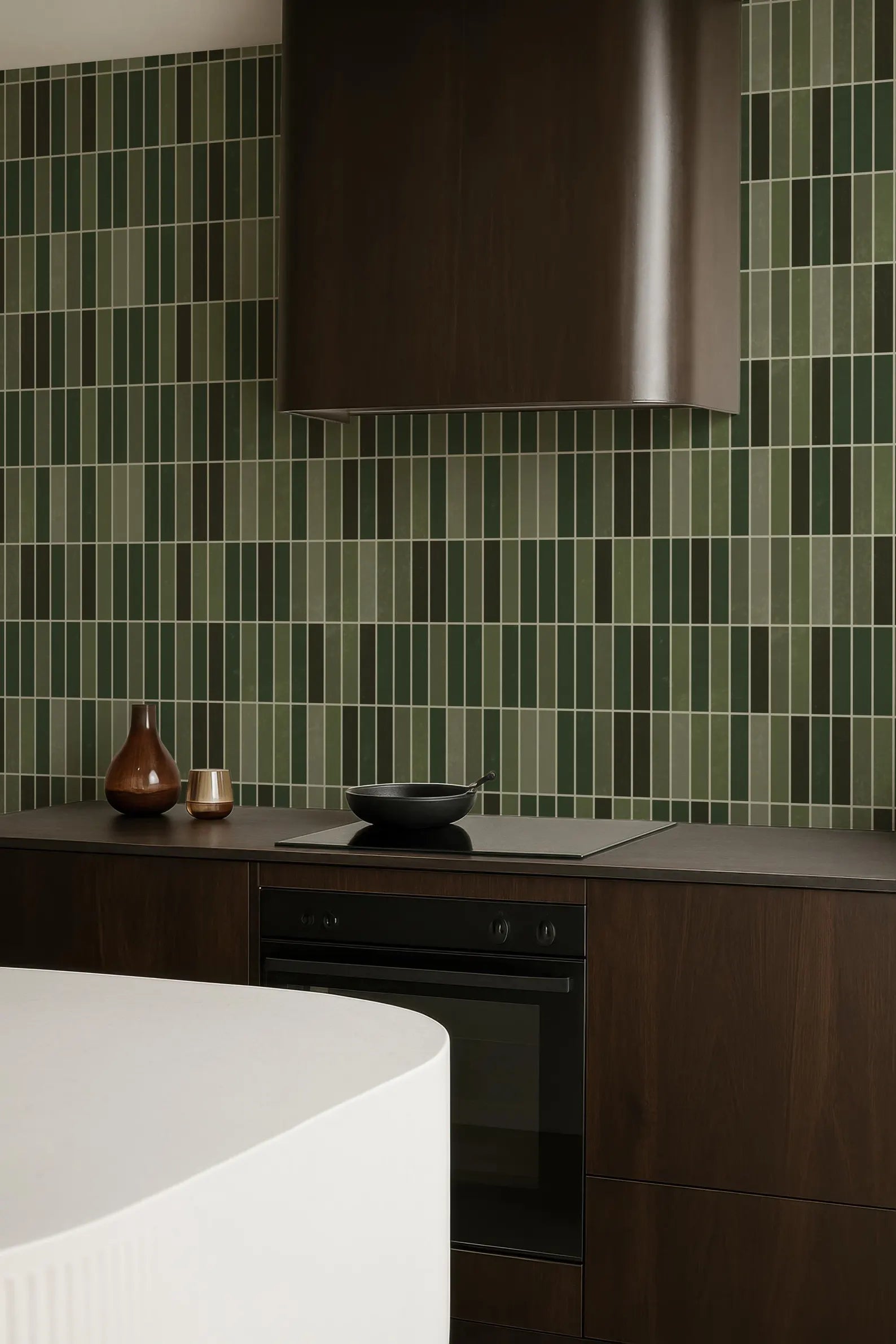 a modern kitchen with a dark wood cabinet, a white countertop, and a black oven. The walls are covered in green and white tiles, creating a vibrant and lively atmosphere.