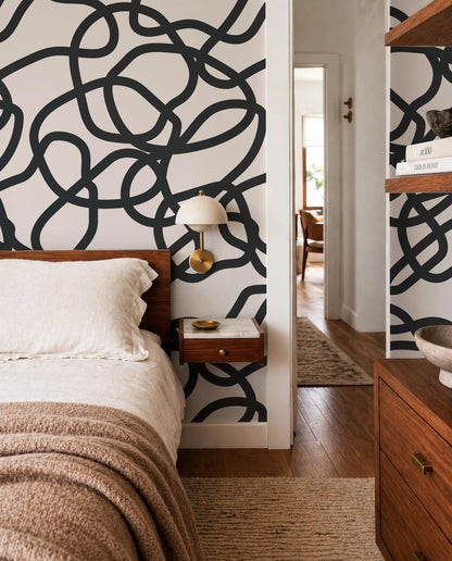a modern bedroom with a large black and white abstract design on the wall behind the bed. The room has a wooden dresser and a nightstand with a lamp, creating a cozy and stylish atmosphere.