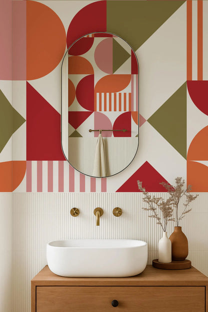 a modern bathroom with a white sink, a large oval mirror, and a wooden cabinet. The walls are adorned with a geometric pattern in shades of red, orange, and green. The bathroom also includes a vase with dried flowers and a potted plant, adding a touch of nature to the space.