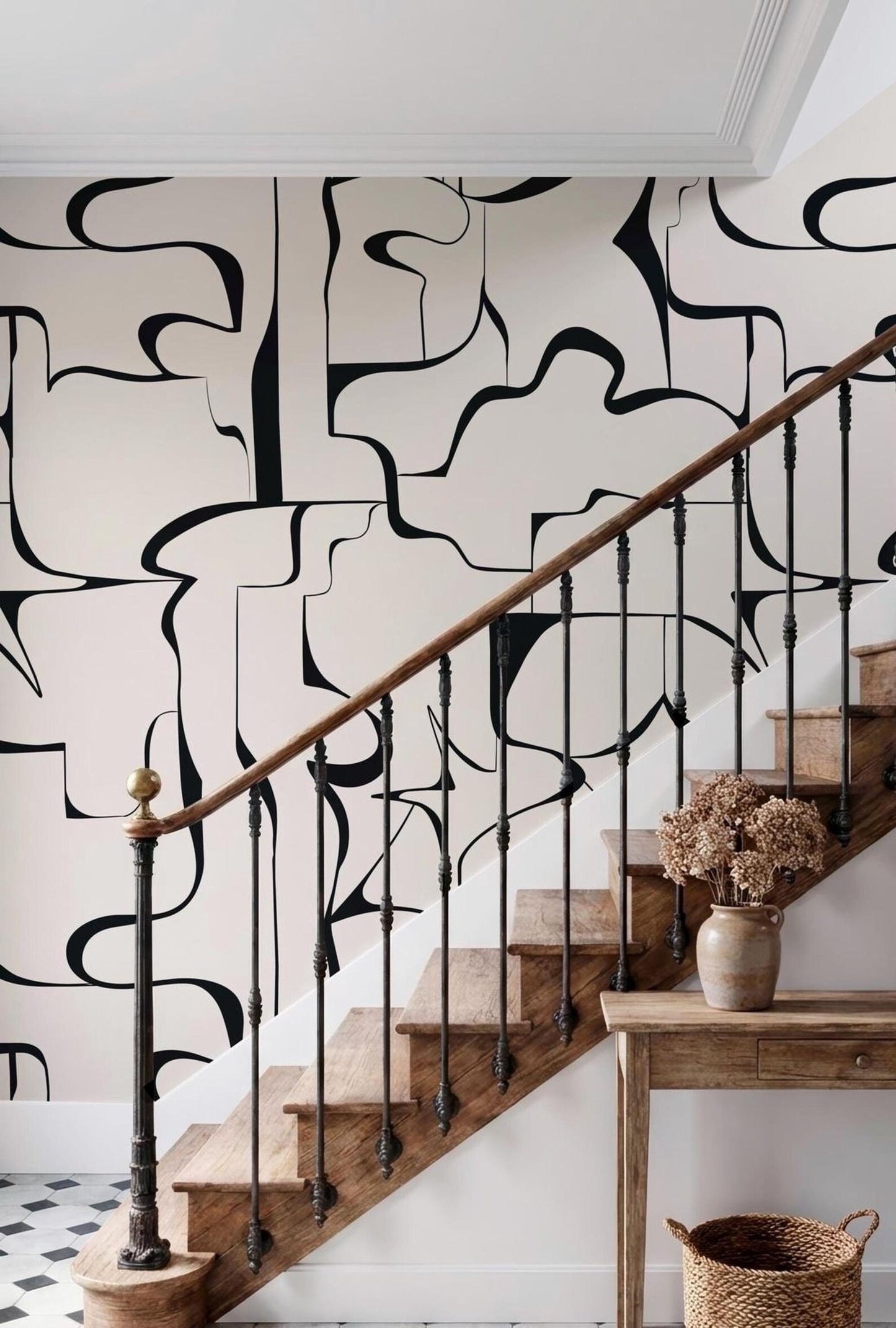 a wooden staircase with a black and white abstract pattern on the wall behind it. The staircase has a wooden railing and a small table with a vase of flowers on it.