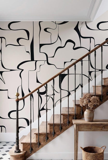 a wooden staircase with a black and white abstract pattern on the wall behind it. The staircase has a wooden railing and a small table with a vase of flowers on it.