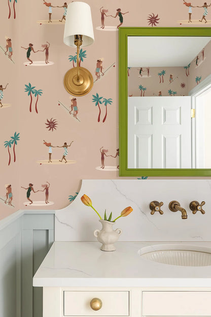 a bathroom with a white sink, a mirror, and a light fixture. The wall behind the sink has a pattern of palm trees and people surfing. There is a vase with flowers on the countertop, and a lamp is also present in the bathroom.