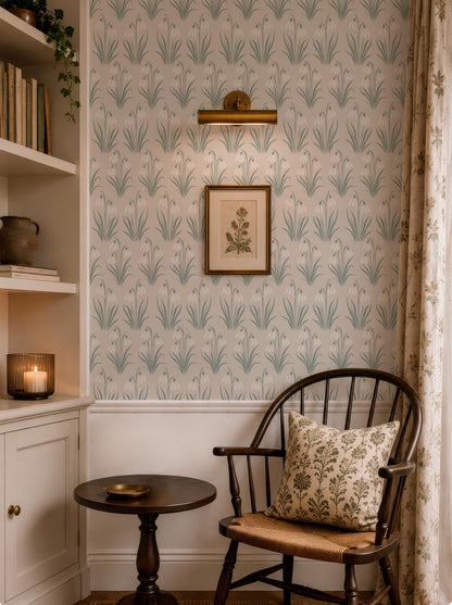 a cozy corner of a room with a wooden chair, a small round table, and a framed picture on the wall. The room has a patterned wallpaper and a bookshelf filled with books and decorative items.