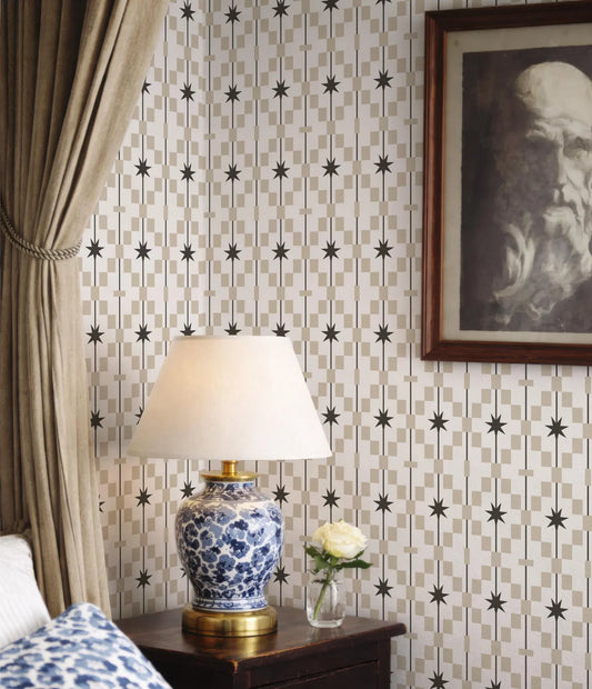 a bedroom setting with a blue and white patterned lamp on a wooden nightstand, a framed portrait of a man on the wall, and a white rose in a vase.