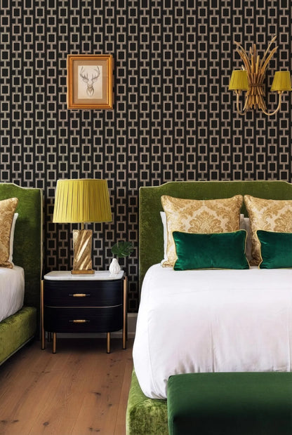 a stylish bedroom with a large bed, a nightstand, and a lamp. The bed has a white comforter and green and gold throw pillows. The nightstand has a black and gold design, and there is a framed picture on the wall above it. The room has a black and white geometric wallpaper pattern, and there is a gold lamp on the nightstand.