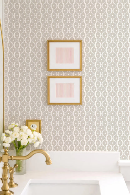 a bathroom with a white sink, a gold faucet, and a framed picture on the wall above the sink. There is also a vase of white flowers on the counter.