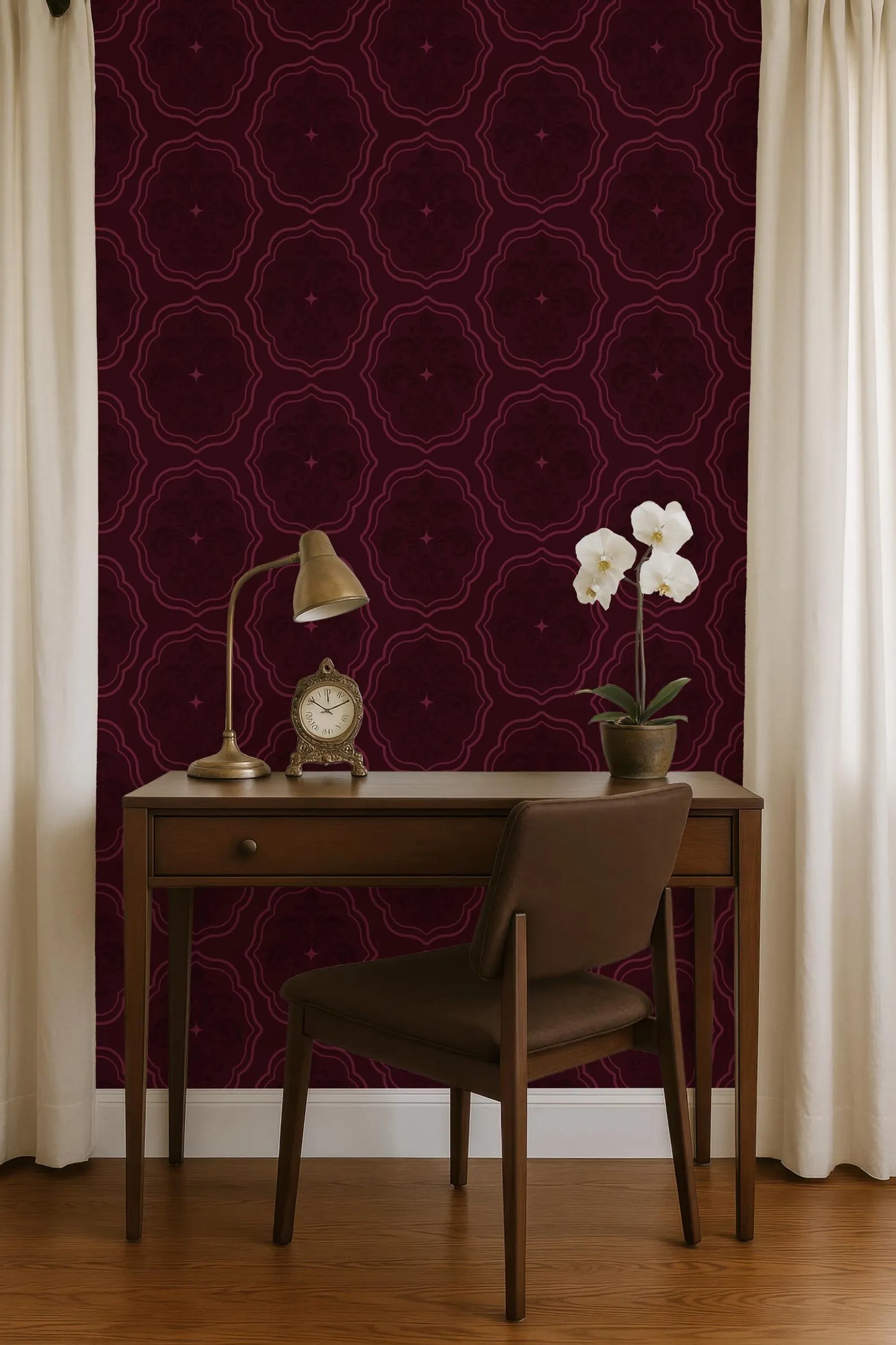 a wooden desk with a lamp, a clock, and a vase of white flowers, set against a burgundy patterned wall.