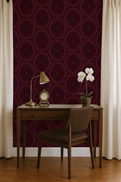 a wooden desk with a lamp, a clock, and a vase of white flowers, set against a burgundy patterned wall.