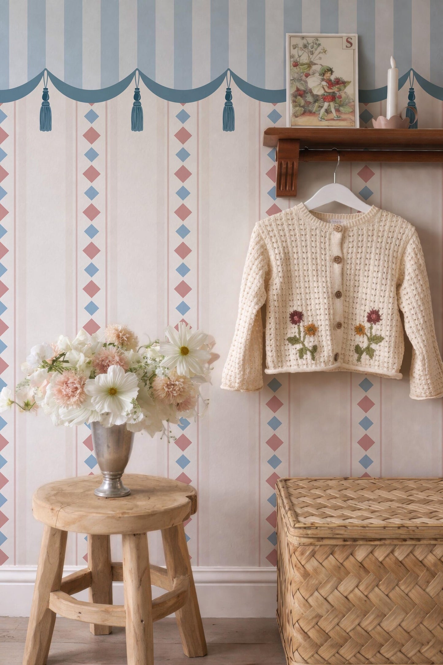 a cozy and charming interior with a wooden stool, a vase of flowers, and a sweater hanging on a wooden rack. The wall behind the furniture is decorated with a patterned wallpaper, and there is a picture frame on the wall.