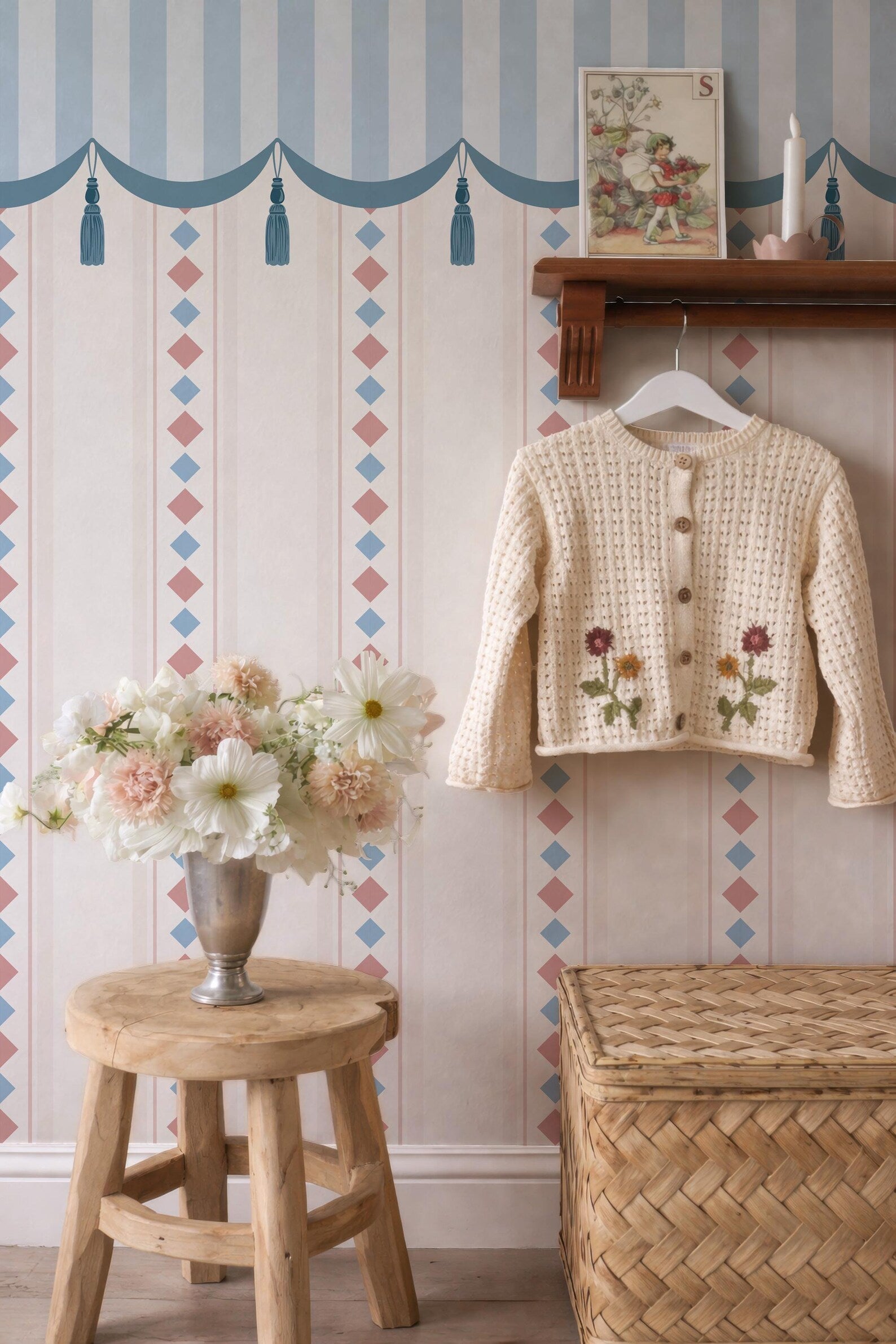 a cozy and charming interior with a wooden stool, a vase of flowers, and a sweater hanging on a wooden rack. The wall behind the furniture is decorated with a patterned wallpaper, and there is a picture frame on the wall.