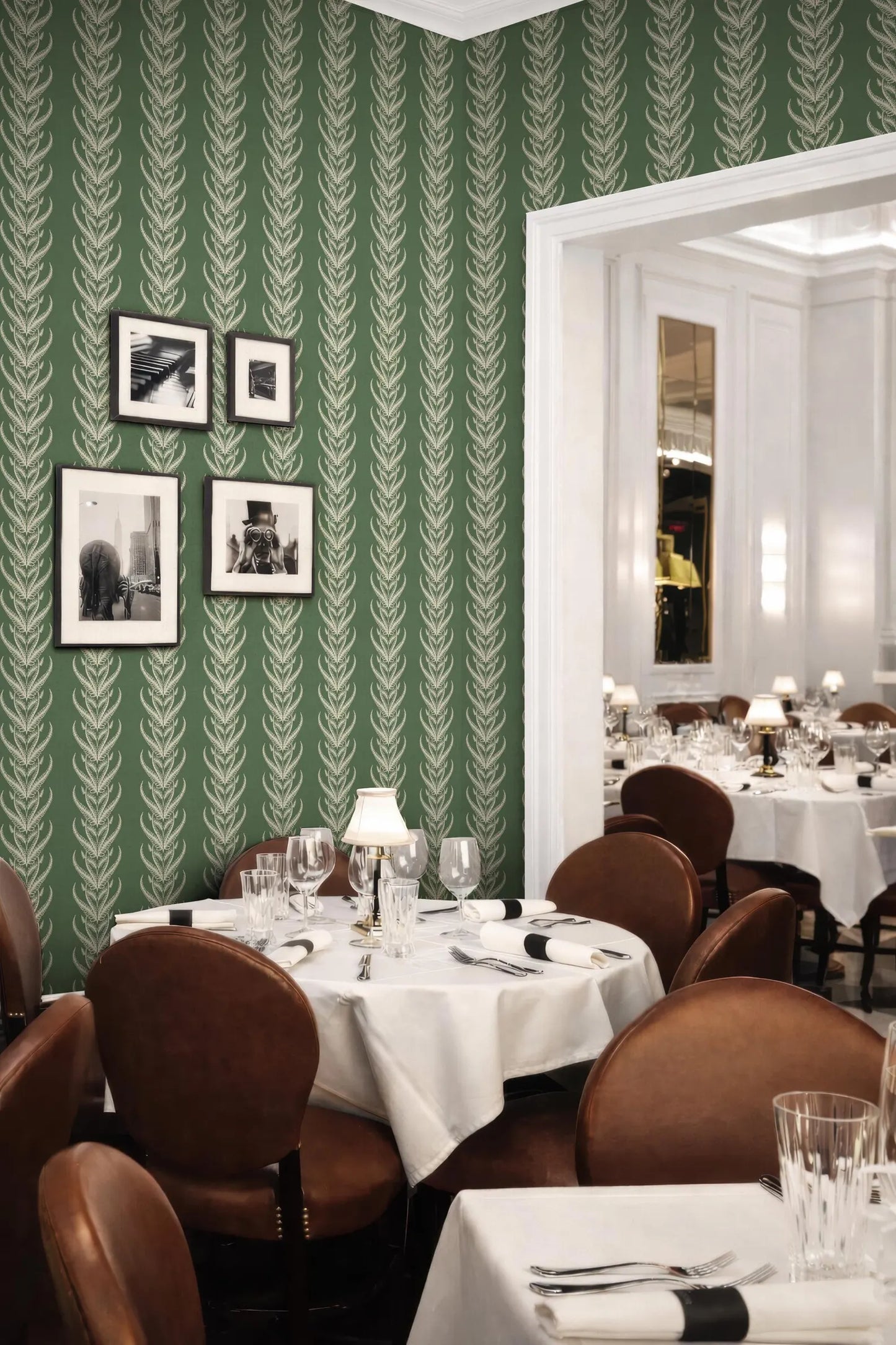 a dining room with a green and white patterned wallpaper, a large mirror, and several tables set with white tablecloths, silverware, and glasses.