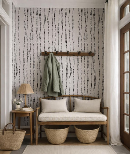 a cozy entryway with a bench, a coat rack, and a lamp. The wall behind the bench has a black and white striped pattern, and there are two woven baskets on the floor next to the bench.