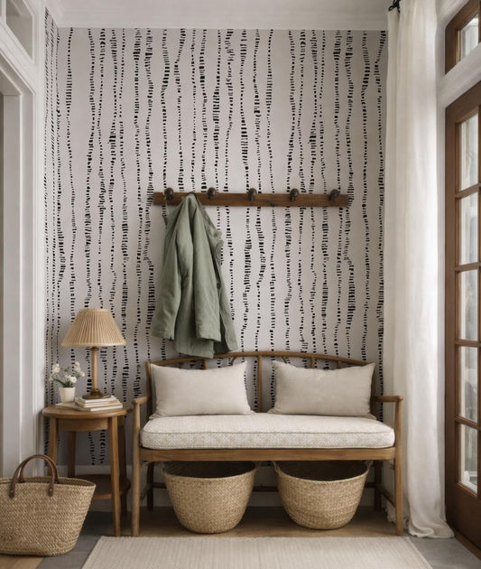 a cozy entryway with a bench, a coat rack, and a lamp. The wall behind the bench has a black and white striped pattern, and there are two woven baskets on the floor next to the bench.