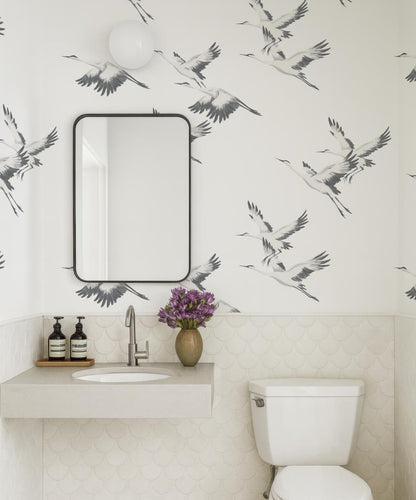 a bathroom with a white sink, a mirror, and a toilet. The walls are decorated with a black and white bird wallpaper, and there is a vase of purple flowers on the counter.