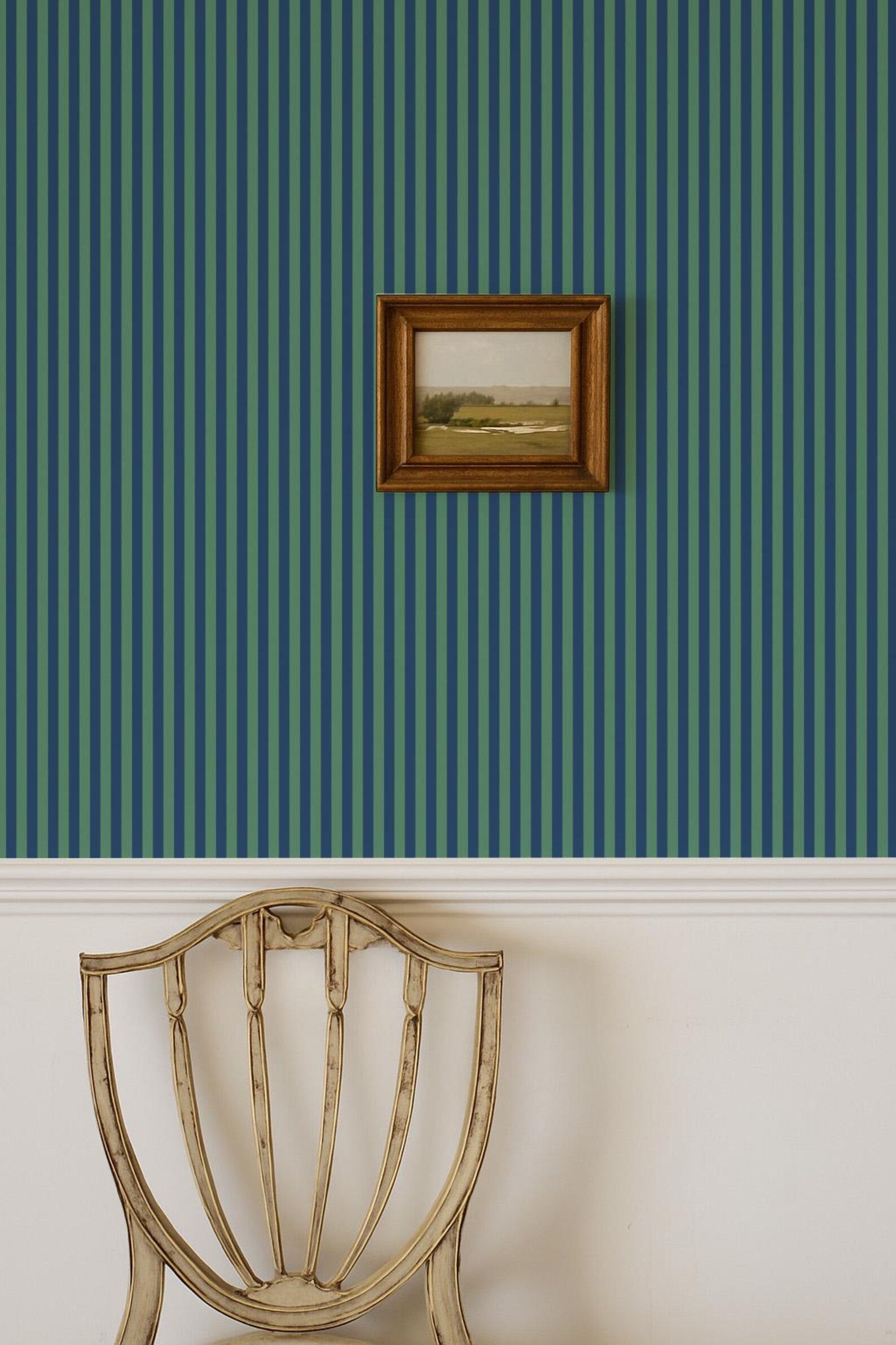 a wooden chair with a white cushion, positioned against a wall with vertical green and blue striped wallpaper. A framed picture is hanging on the wall above the chair.