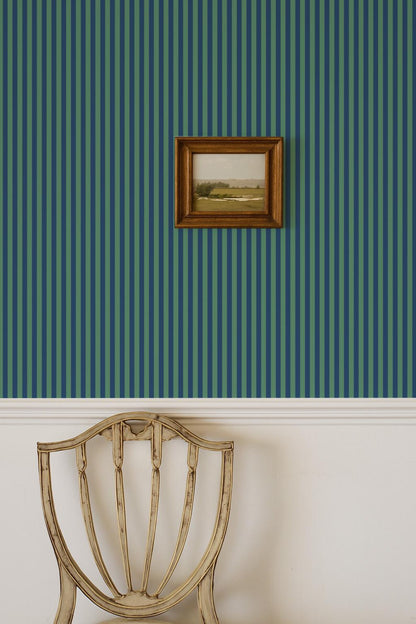a wooden chair with a white cushion, positioned against a wall with vertical green and blue striped wallpaper. A framed picture is hanging on the wall above the chair.