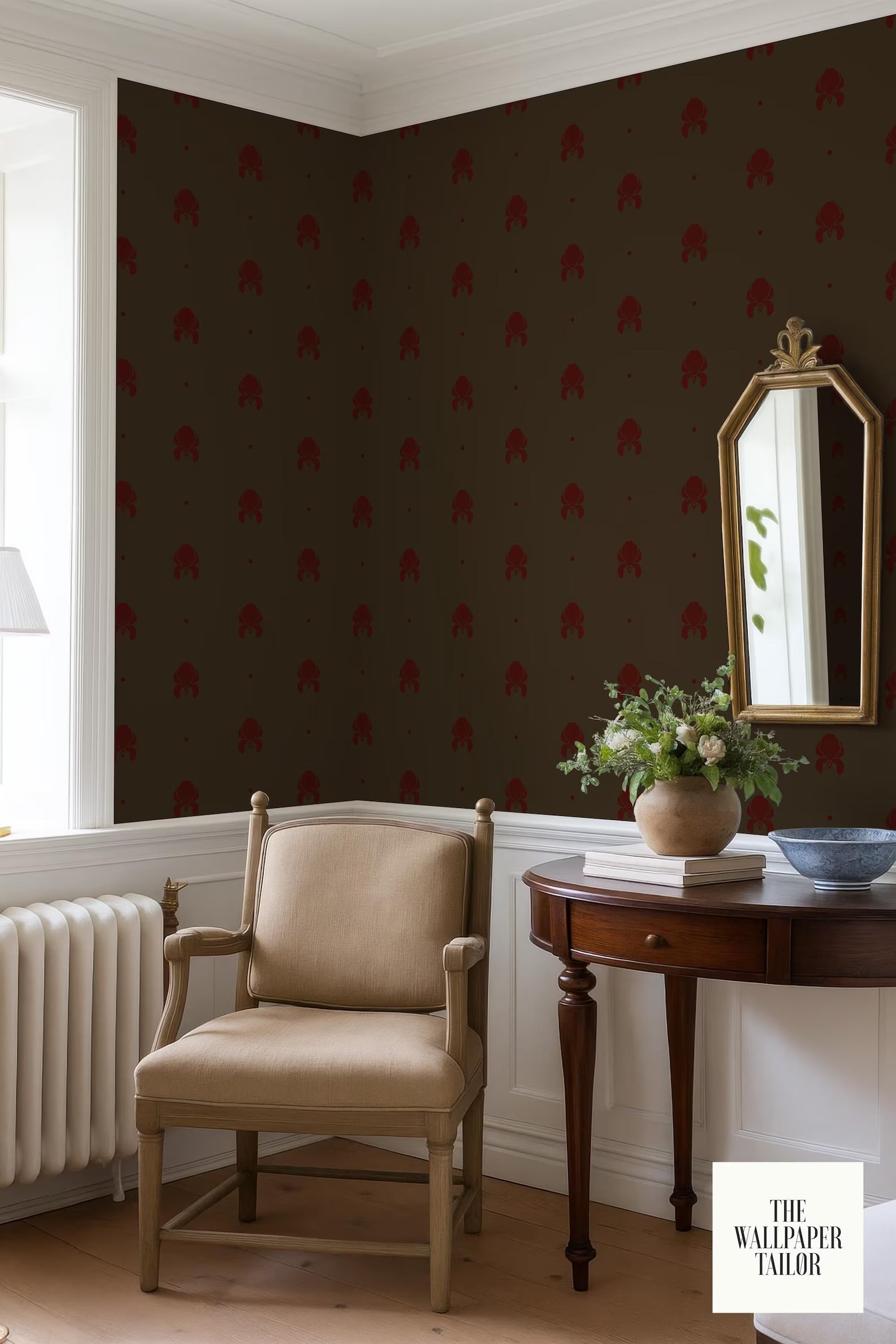 a cozy corner of a room with a beige armchair, a wooden side table with a vase of flowers, and a mirror on the wall. The wall has a dark brown pattern with red accents, and there is a window in the background.