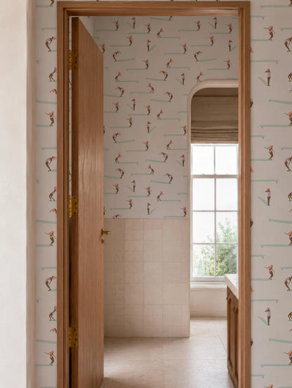 a bathroom with a wooden door, a patterned wallpaper, and a window. The door is open, revealing a glimpse of the hallway beyond.
