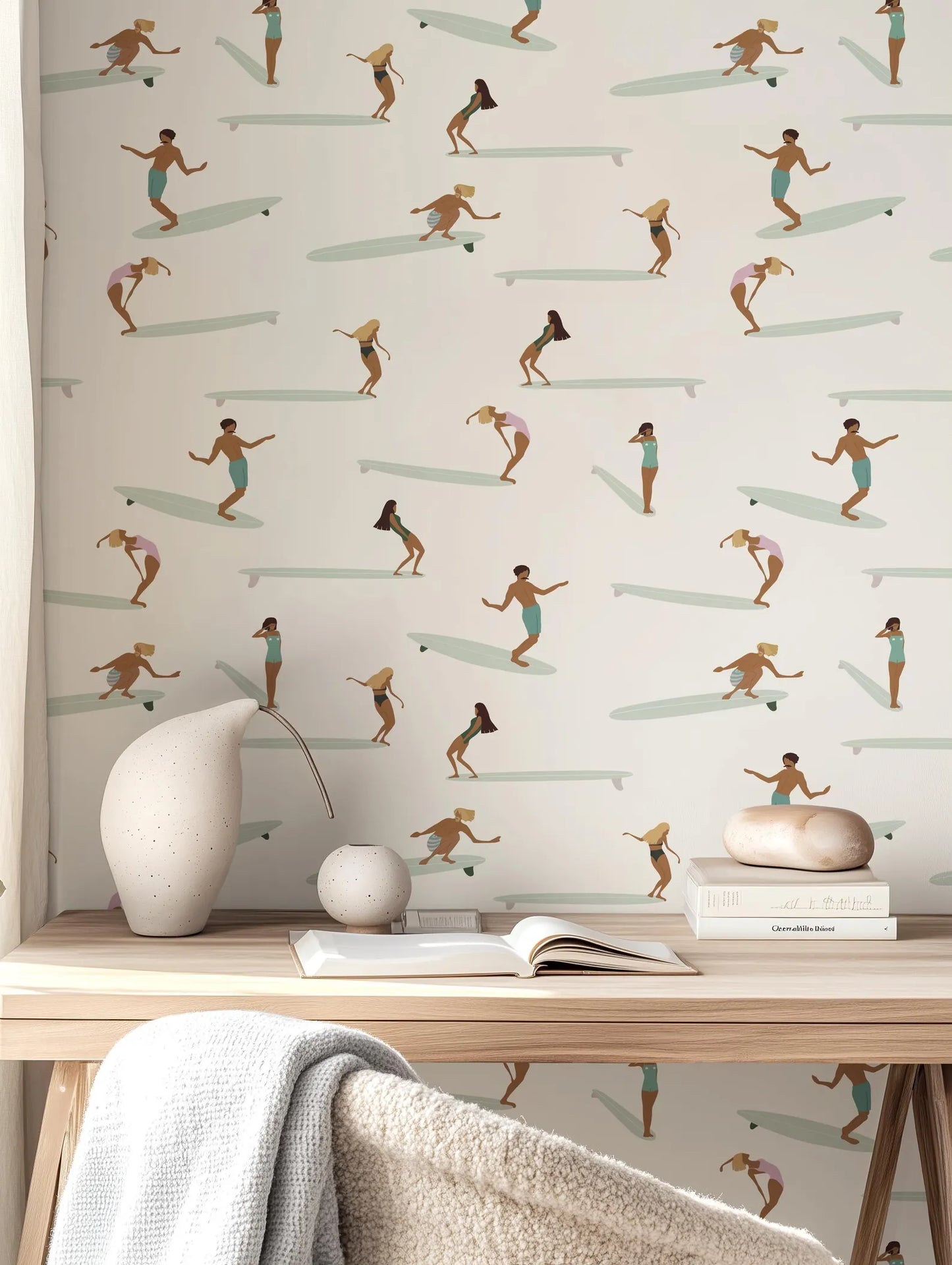 a wallpapered wall with a repeating pattern of people surfing on surfboards. In the foreground, there is a wooden desk with a white vase, a book, and a small white figurine.