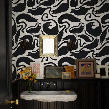 a bathroom with a black and white cat wallpaper, a white sink, and a shelf with framed pictures and a vase of sunflowers.