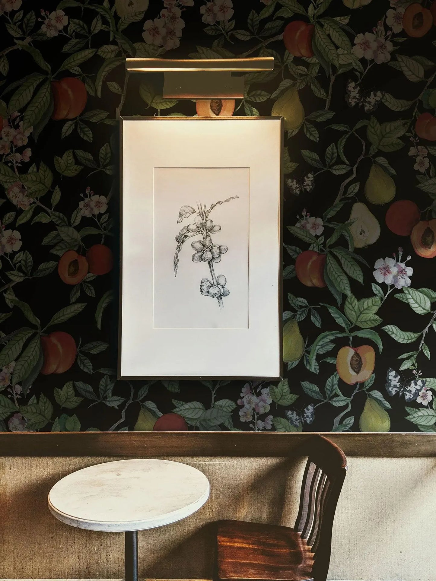 a black and white drawing of a flower on a wall, with a framed artwork hanging above a small round table and a wooden chair.