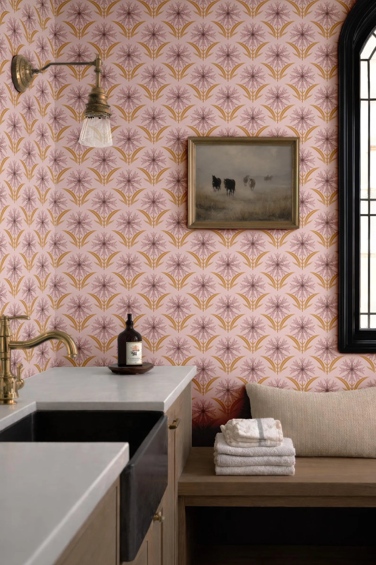 a bathroom with a pink and gold floral wallpaper, a sink, a mirror, a wooden bench, and a framed picture of cows on the wall.