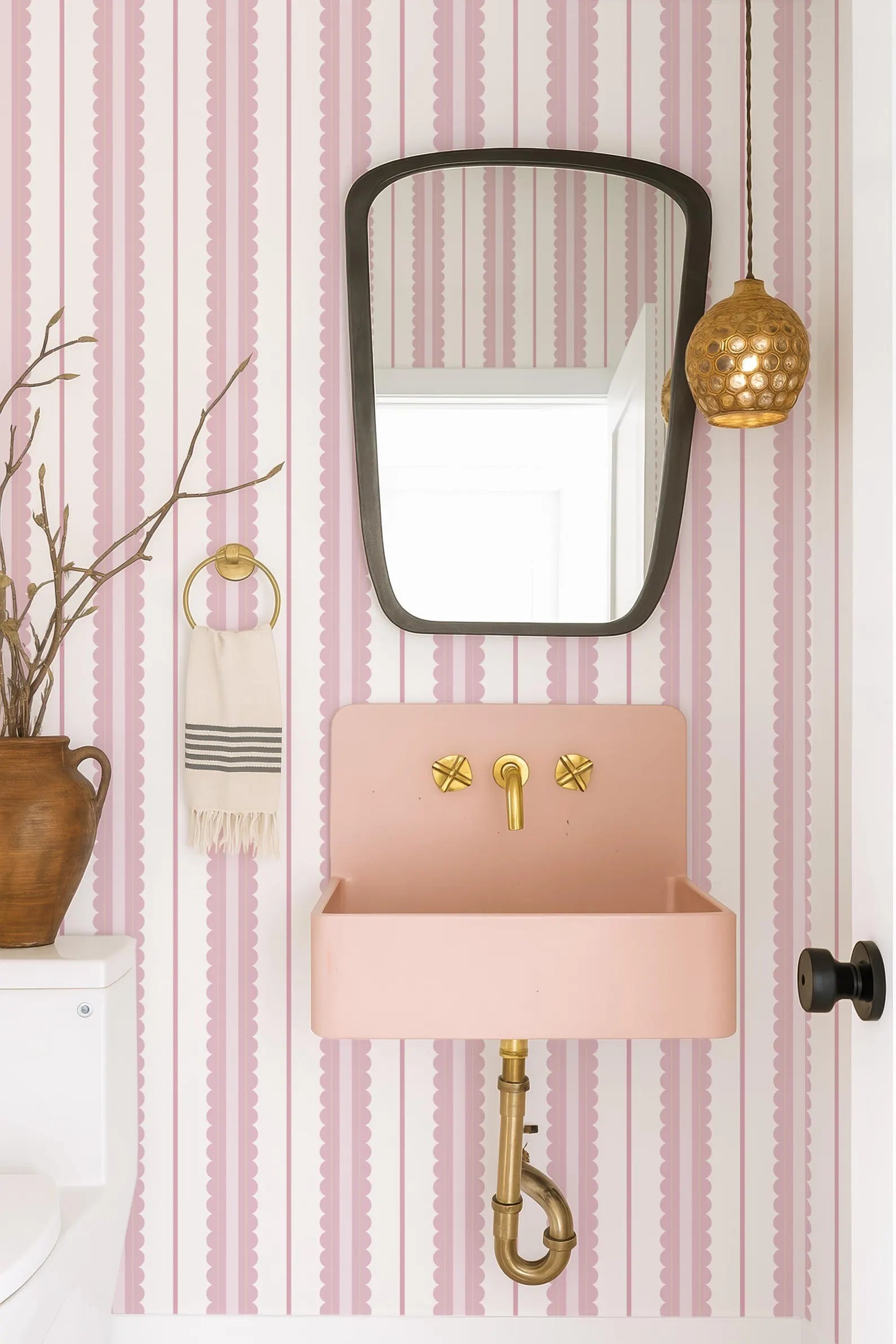 a bathroom with pink and white striped wallpaper, a pink sink, a mirror, and a hanging light fixture.