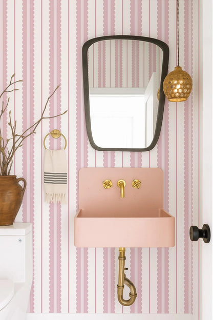 a bathroom with pink and white striped wallpaper, a pink sink, a mirror, and a hanging light fixture.