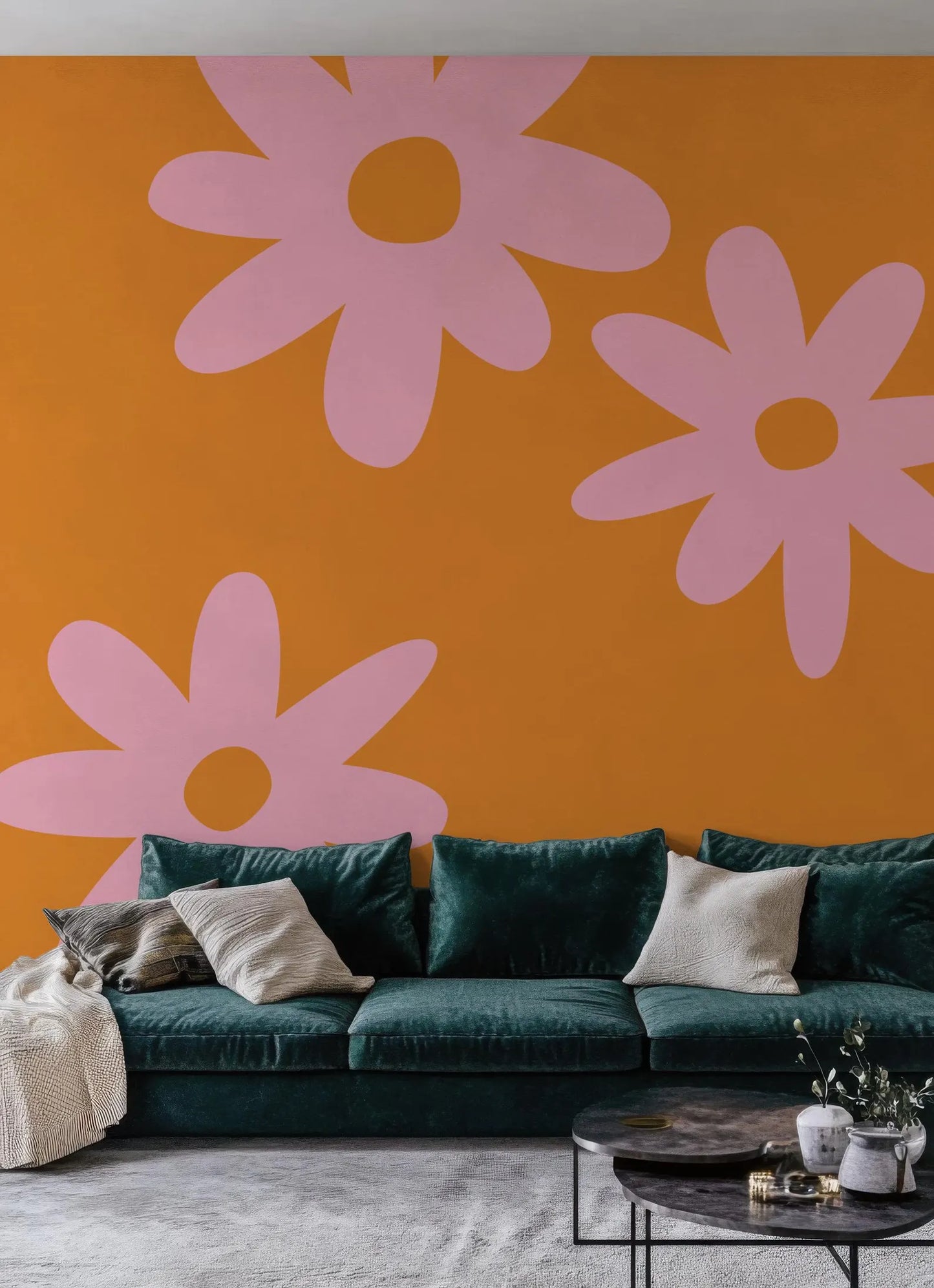 a living room with a green velvet sofa and a coffee table. The walls are painted in a vibrant orange color, and there are three large pink flower-like designs on the wall.