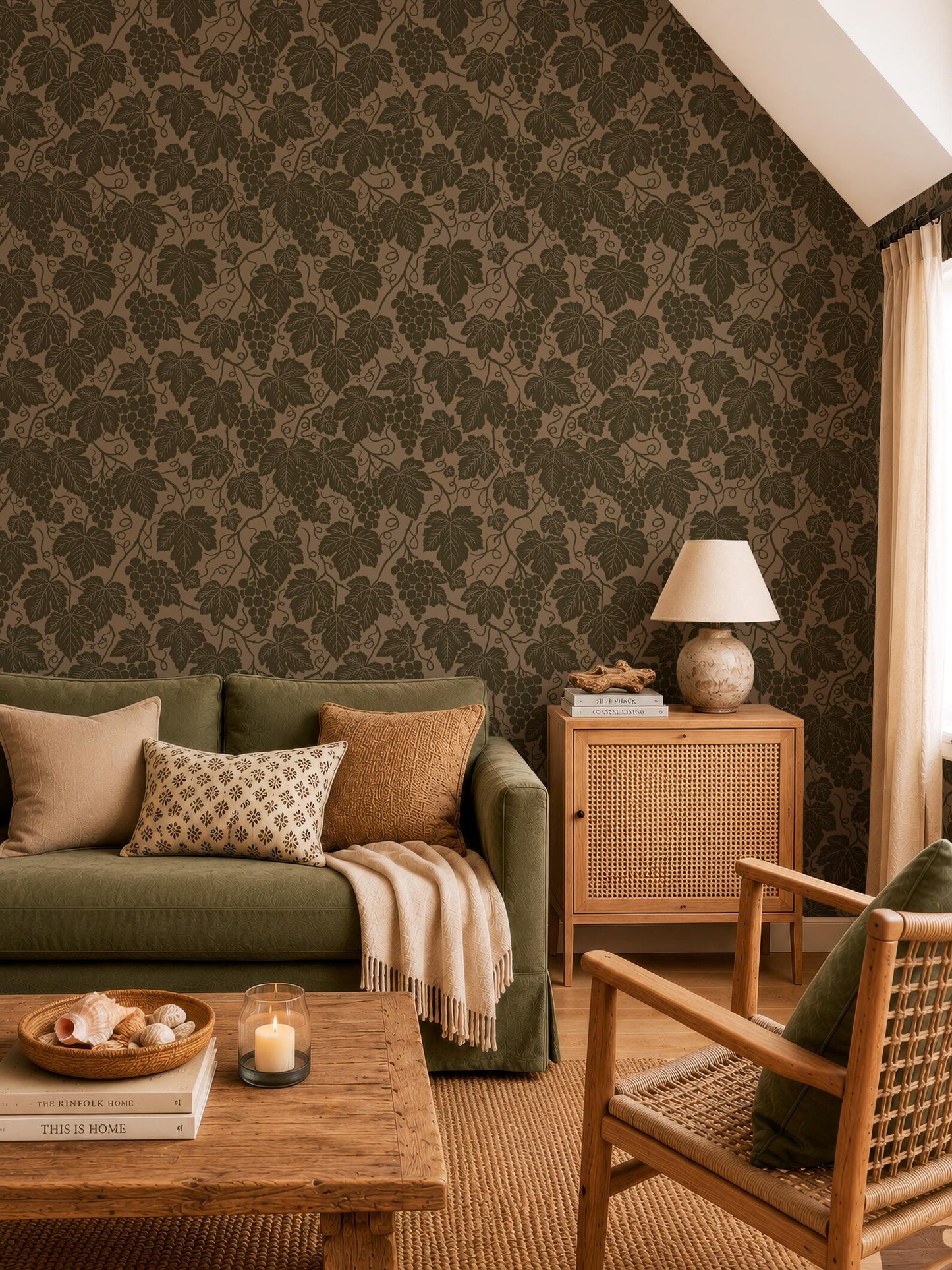 a cozy living room with a green sofa, a wooden coffee table, and a woven chair. The walls are covered in a patterned wallpaper with a repeating leaf design. The room has a warm and inviting atmosphere, with a lamp, books, and a bowl of fruit on the coffee table.