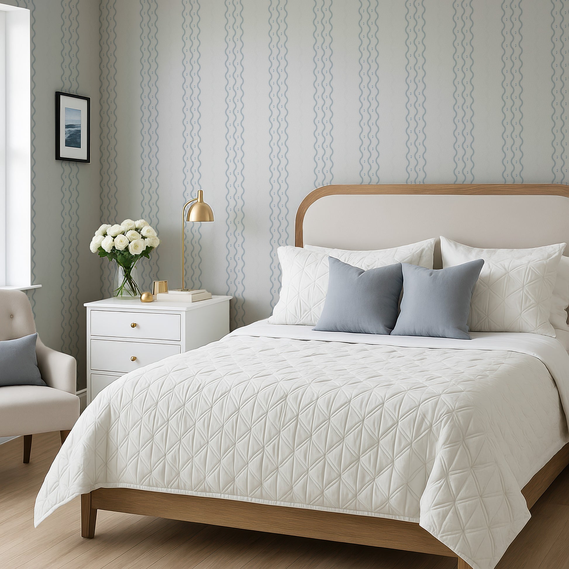 a well-furnished bedroom with a large bed, a nightstand, and a chair. The bed has a white comforter and a wooden headboard, and the room has a neutral color scheme with gray and white walls and a wooden floor.