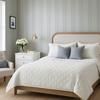 a well-furnished bedroom with a large bed, a nightstand, and a chair. The bed has a white comforter and a wooden headboard, and the room has a neutral color scheme with gray and white walls and a wooden floor.