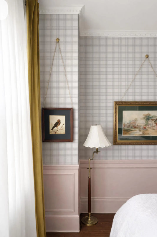 a bedroom with a bed, a lamp, and two framed pictures hanging on the wall. The room has a checkered wallpaper and a pink wall, creating a cozy and inviting atmosphere.