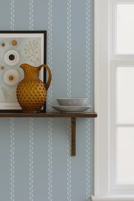 a shelf with a brown vase, a white bowl, and a framed picture on it, set against a blue wall with white stripes.