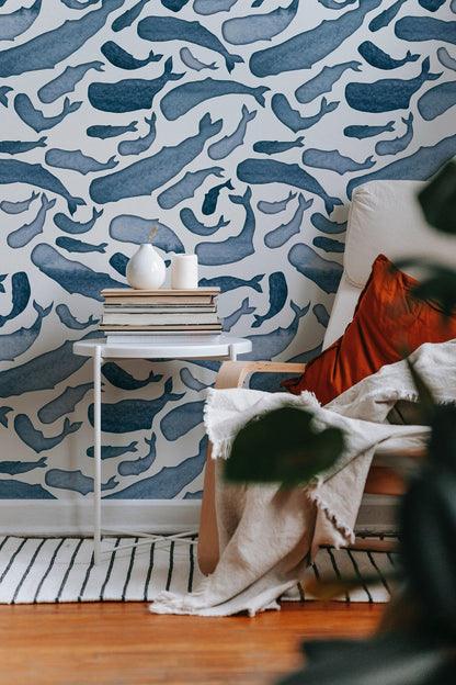 a cozy living space with a white armchair, a white side table, and a patterned wallpaper with blue whale illustrations. The room has a wooden floor and a striped rug, creating a warm and inviting atmosphere.