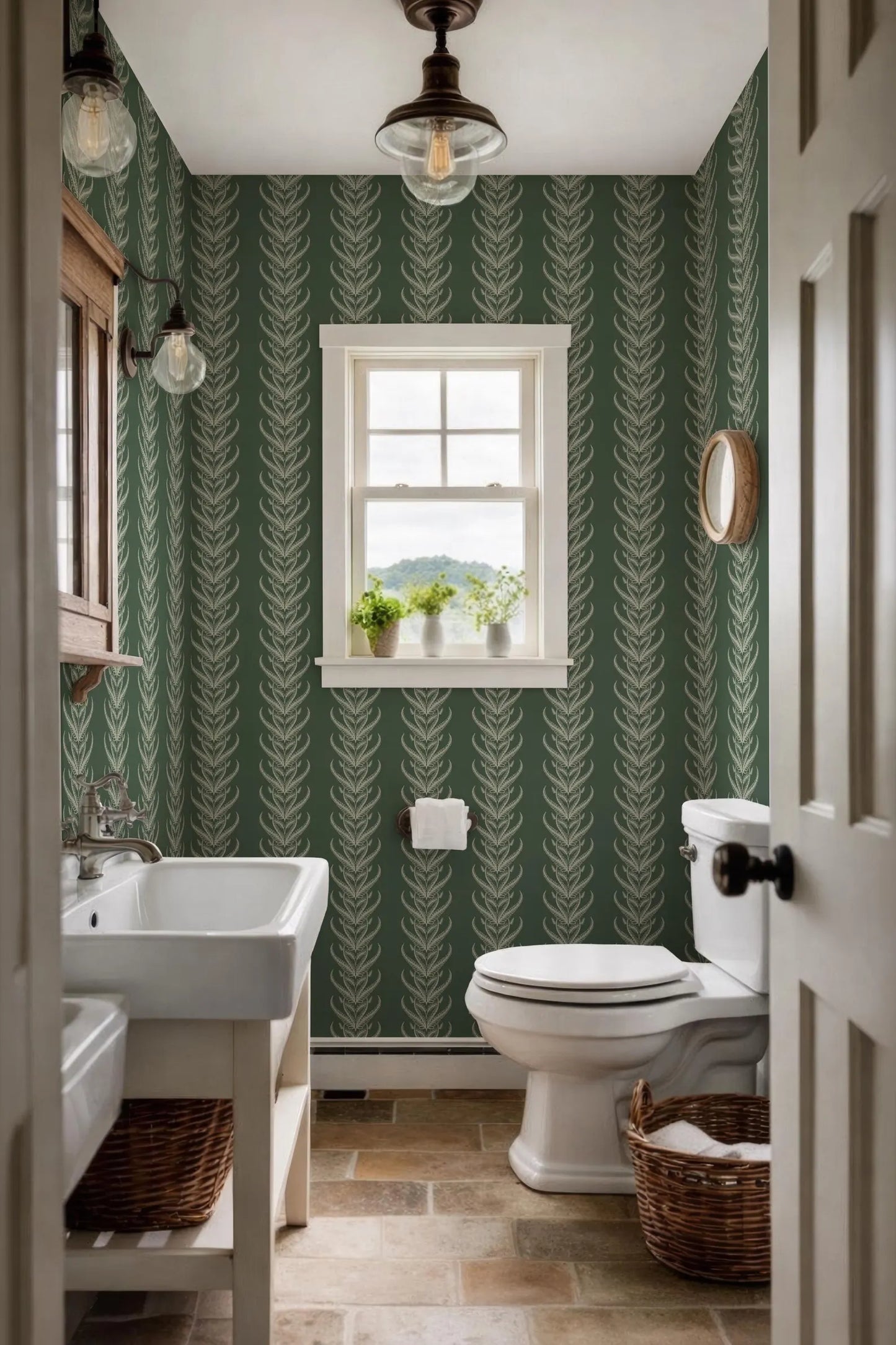 a small bathroom with a white sink, toilet, and a window with a view of the outdoors. The walls are covered in a green and white patterned wallpaper, and the floor is made of tiles. There is a basket on the floor next to the toilet.