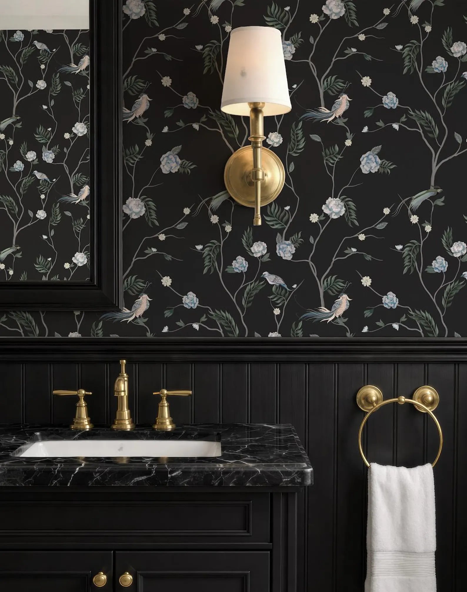 a bathroom with a black and white floral wallpaper, a black marble vanity with gold faucets, and a gold towel ring.